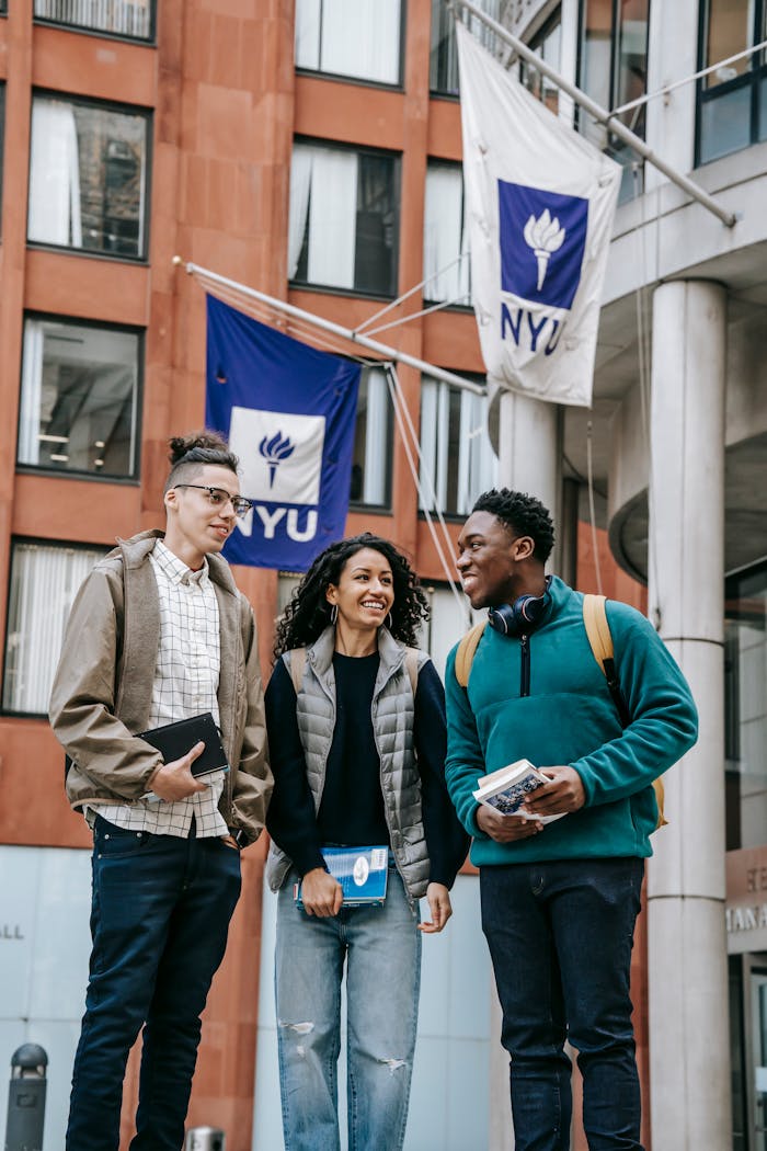 Happy multiracial students smiling near modern building with flags on urban street in daytime